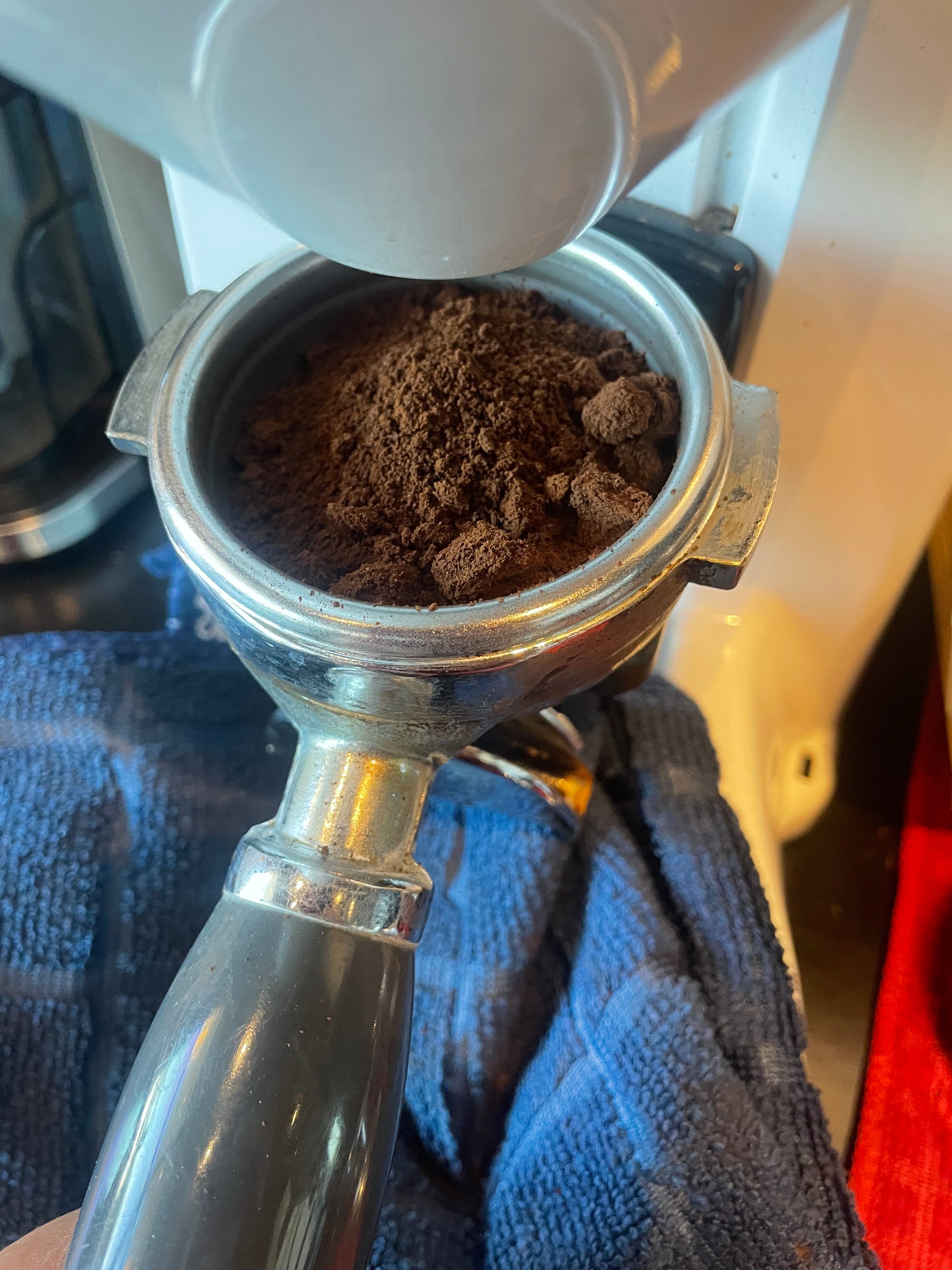 Close-up of a coffee grinder with ground coffee inside, on a blue towel.